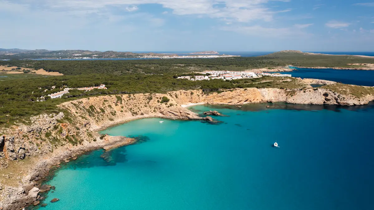 Velero navegando en las aguas turquesas de una de las calas secretas de Menorca