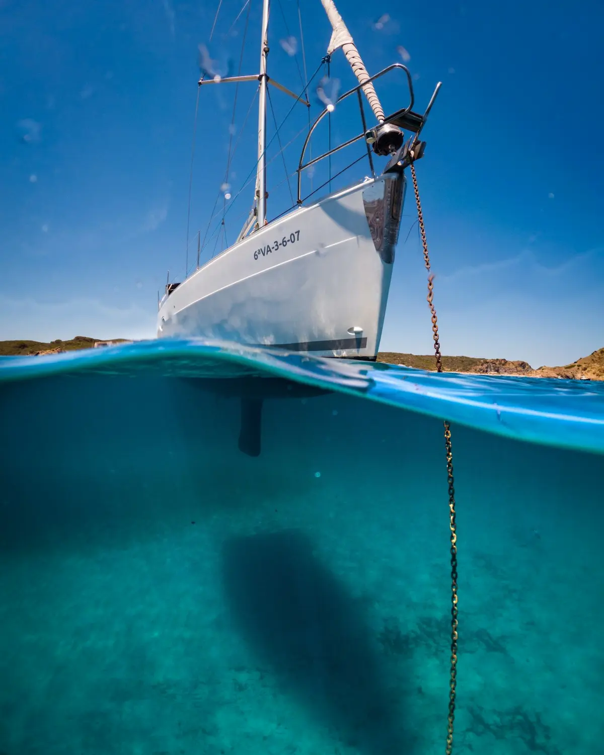 Hull of the sailboat anchored over crystal-clear water in Menorca, half-underwater view
