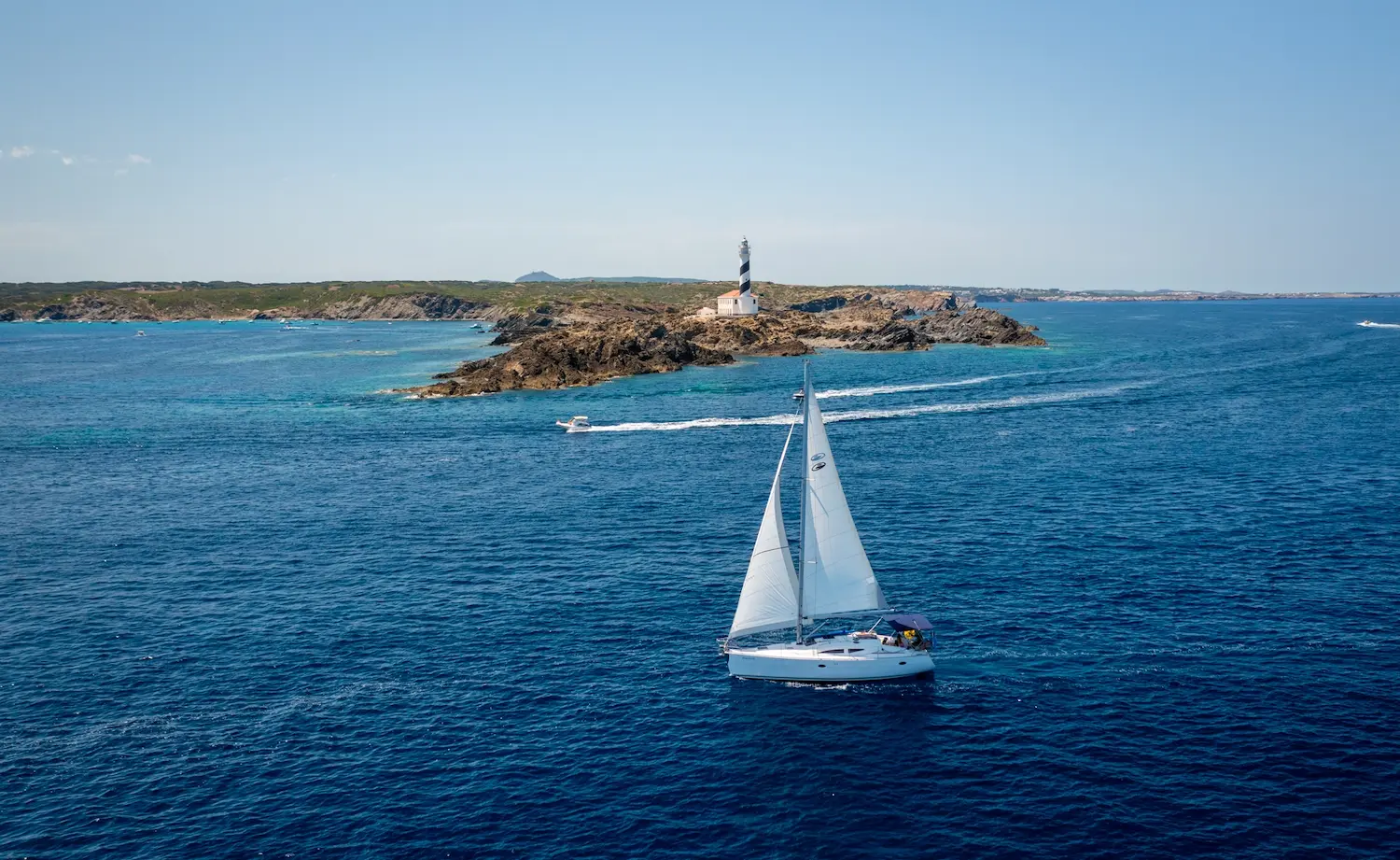 Velero navegando frente al faro de la Isla del Aire en Menorca