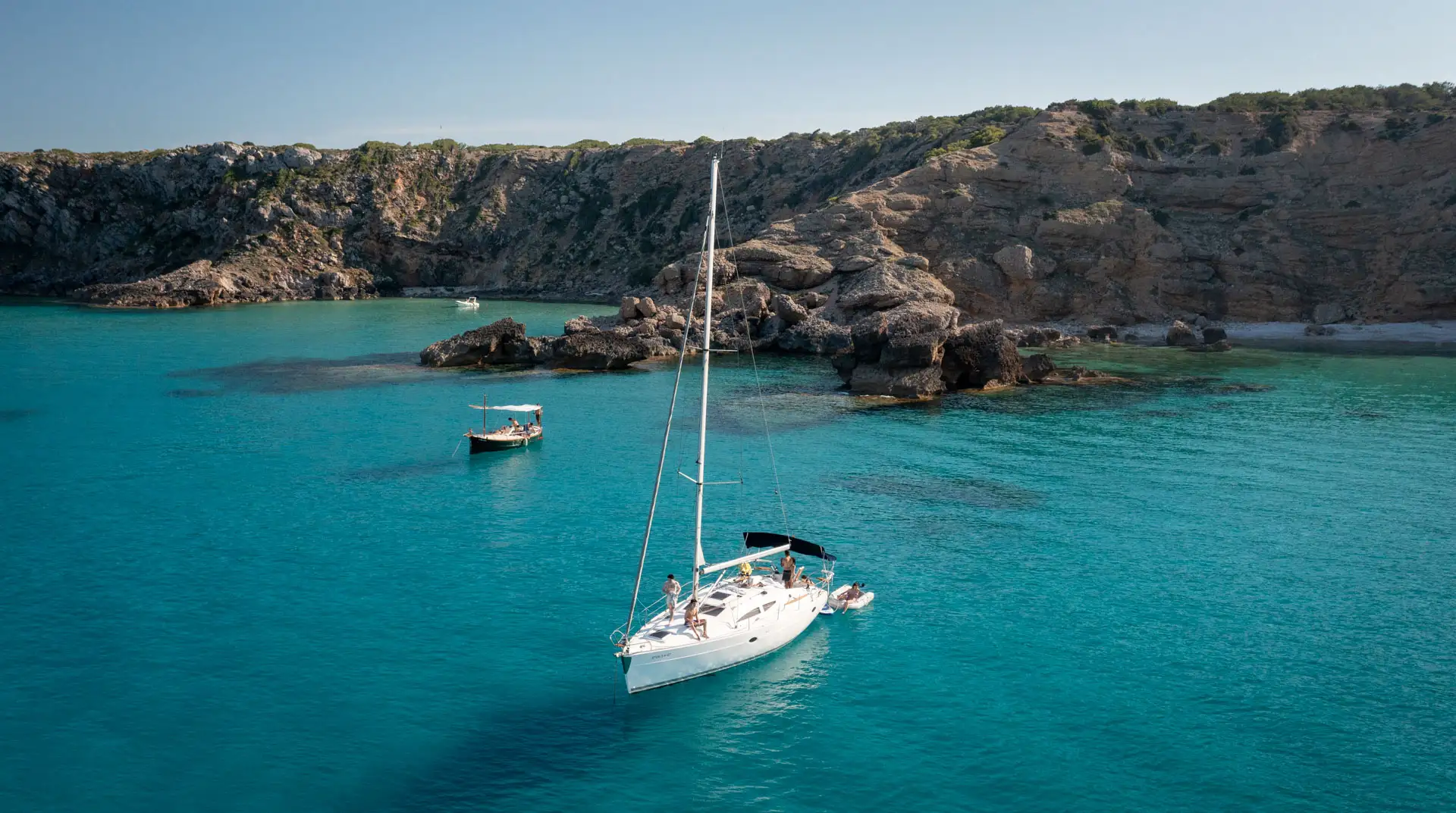 Velero navegando a vela con el patrón al timón por la costa de Menorca