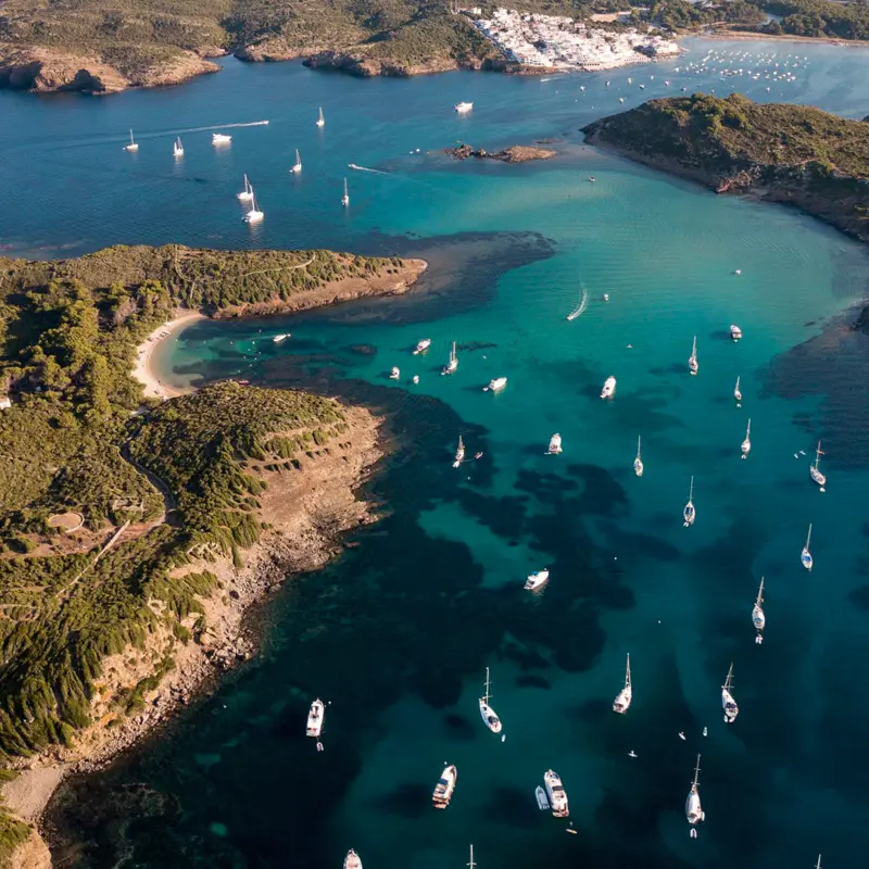 Vista aérea de veleros fondeados en las aguas turquesas del canal de la Illa d'en Colom, en Menorca